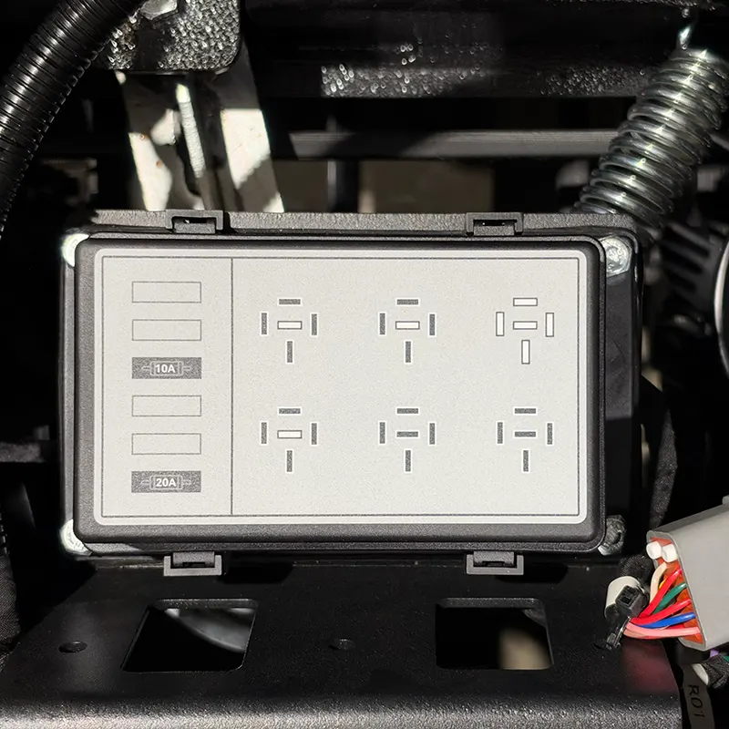 A close-up of a car fuse box cover with printed fuse and relay positions, surrounded by black wiring and connectors.