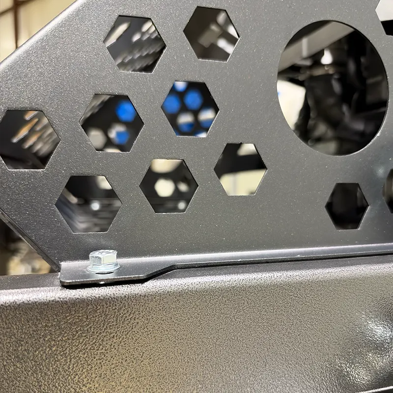A black perforated metal panel with hexagonal and circular cutouts, attached with a silver bolt over a textured gray surface.